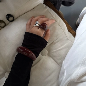 Dettaglio di un set di bracciale e anelli in resina bordeaux indossato su manica nera