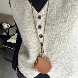 Détail du porte-lunettes de soleil en cuir marron avec bouton pression et surpiqûres blanches