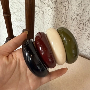 Dettaglio di ampi bracciali in resina neri, rossi, crema e verde oliva con finitura lucida