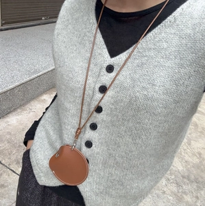 Gros plan d'un collier porte-lunettes en cuir marron avec cordon tressé sur un gilet gris
