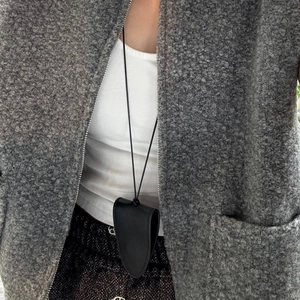 Détail du collier porte-lunettes en cuir noir avec coutures fines sur manteau gris