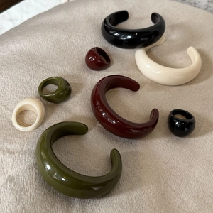 Dettagli di bracciali in resina verde oliva e bordeaux lucidi su un fondo di lino