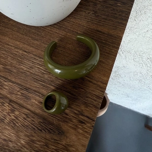 Set di gioielli in resina verde oliva con bracciale aperto e anello su tavolo in legno