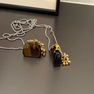 Detail of mini bag pendants in tiger eye and black stone with gold metal accents