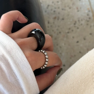 Detail eines schwarzen Harzrings und eines silbernen Kugelkettenrings am Finger
