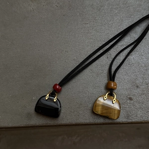 Detail of stone handbag pendants in black onyx and tiger eye with golden metal accents