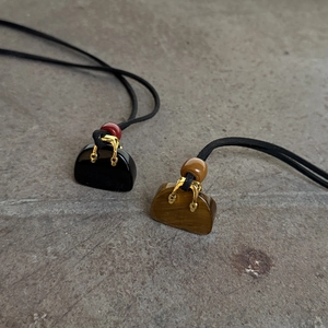 Macro detail of bag-shaped stone pendants with gold handles on minimalist black cord