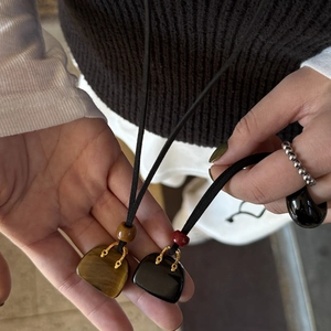 Detail of tiger eye and black stone mini bag pendants with gold handles on a necklace