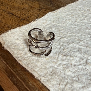 Detail eines silbernen, mehrlagigen Wickelrings mit offenem Band auf strukturiertem Papier