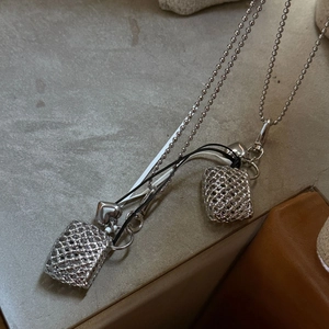 Macro detail of silver woven purse pendant with heart charm on a metal bead chain