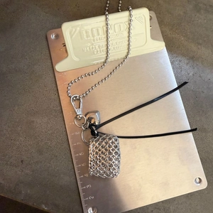Macro shot of silver woven metal bag pendant necklace with a heart charm on a metal board