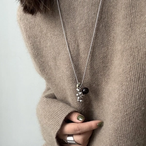 Detail of long titanium steel necklace with natural stone beads on a brown sweater