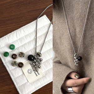Beaded natural stone sweater necklace with silver spheres and black pendant on wood background