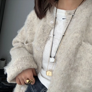 Detail einer minimalistischen Gold Parfümflaschen-Kette und eines flüssigen Metallrings