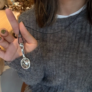 Detalle de un colgante de cuchara con cordón negro sobre un jersey de punto gris