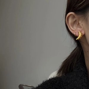 Detail of golden croissant earring and diamond-studded hoop on model in black sweater