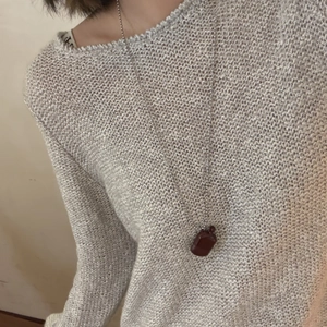 Nahaufnahme der Parfümflaschen-Halskette auf einem grauen Damenstrickpullover