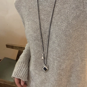 Detail einer mehrlagigen Halskette mit schwarzem Seil und Metallanhängern auf grauem Strick