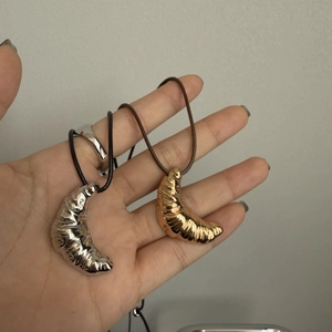Close-up of gold and silver croissant pendants with polished finish on cord necklaces