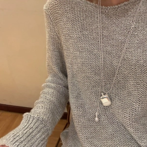 Silberne Parfümflaschen-Halskette kombiniert mit einem grauen grob gestrickten Pullover