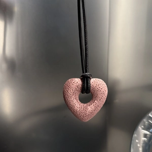 Macro shot of pink heart-shaped lava stone pendant on a minimalist black cord