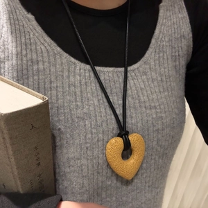 Macro shot of yellow hollow heart lava stone necklace on a grey sweater lifestyle setting