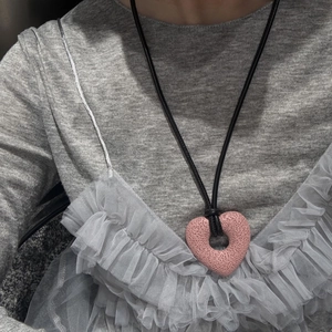 Close-up of pink textured heart pendant on black cord worn over a grey outfit