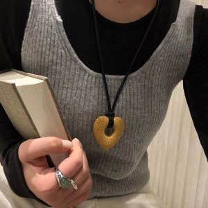 Detail of hollow heart-shaped volcanic stone pendant with black leather cord on a gray sweater