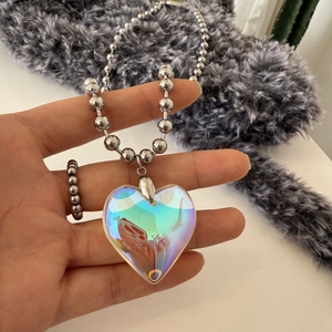 Macro detail of iridescent heart pendant on a silver bead chain held by hand