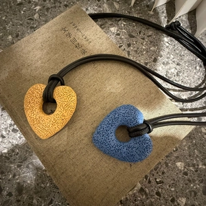 Macro detail of porous lava stone heart pendants with textured finish on black leather cord