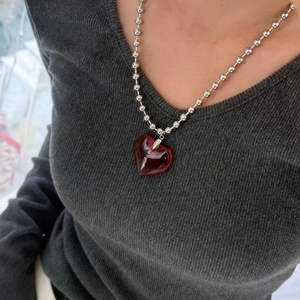 Detail of red heart crystal pendant on a silver ball chain worn over grey fabric