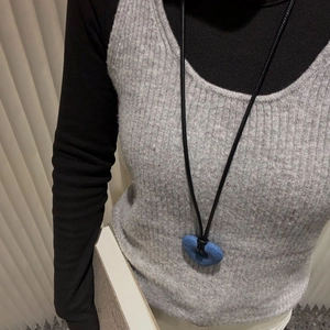 Detail of a blue matte circular pendant on a minimalist long black leather cord necklace