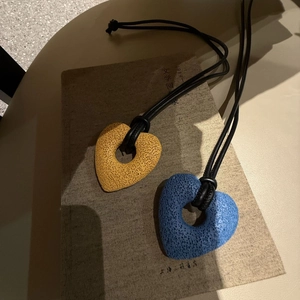 Detailed close-up of yellow and blue heart-shaped porous lava stone pendants on black cords