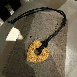 Macro detail of yellow porous heart pendant on a black leather adjustable cord necklace