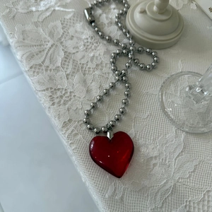 Detailed view of a red crystal heart pendant on a silver ball chain over lace