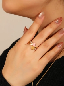 Détail d'une bague double cœur en or rose avec émail rose et cristaux sur le doigt