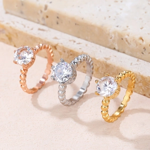 Three twisted band solitaire rings in rose gold, silver, and gold on stone background