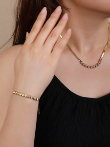 Close-up of gold titanium necklace and bracelet set featuring round zircon stones