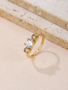 Detail eines Goldrings mit rundem Zirkon und Herzakzenten auf Marmorsteinen
