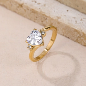 Elegant gold heart ring with white crystal and sparkling side stones on stone surface