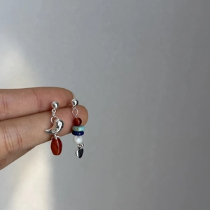 Detailed view of asymmetric earrings with bird and heart charms and colorful beads
