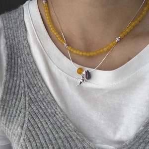 Detail of layered necklace with yellow beads, silver bird pendant and purple droplet charm