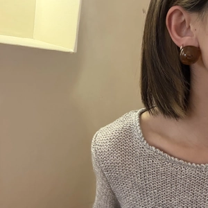 Close-up of translucent brown resin stud earrings worn with a cozy knit sweater