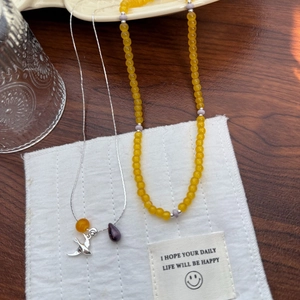 Detail of silver magpie bird pendant and yellow agate bead necklace on fabric