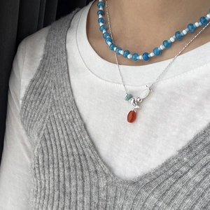 Detail of layered silver chain necklace with blue beads and a red teardrop pendant