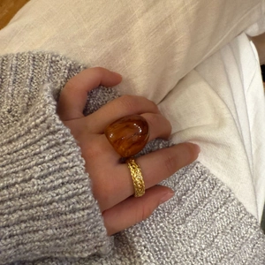 Nahaufnahme eines Bernstein-Harzrings und eines goldenen geflochtenen Metallrings am Finger