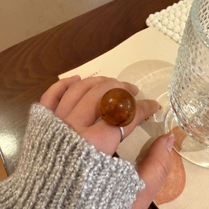 Translucent amber resin ball ring shown on model's hand in a cozy lifestyle setting