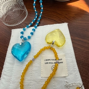 Close-up of translucent heart pendants with matching beaded chains on a wooden surface