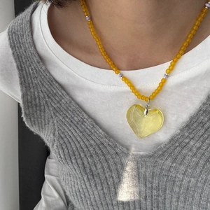 Detailed view of a yellow beaded necklace with a large translucent heart pendant on a model