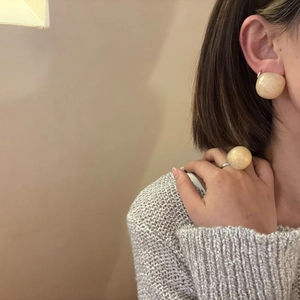 Close-up of translucent beige resin dome ring and matching stud earrings on a model